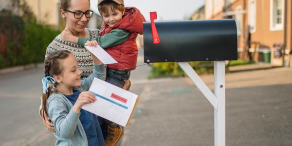 Children with their mother on a street with mailbox mailing ballot.