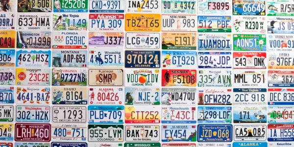 American license plates of various states on the outside wall of a gas station.