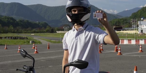 Young person in a helmet on a motorbike showing driving license.
