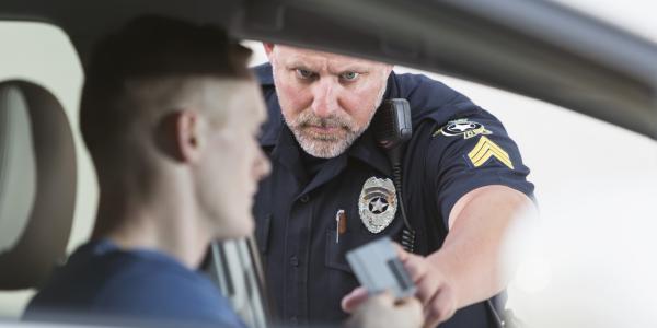 A serious police officer reaching for the ID card of a young driver he pulled over.